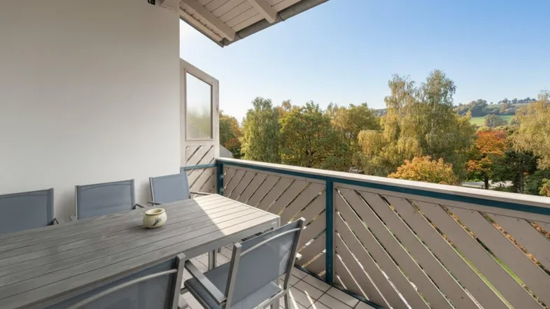 Sonniger Balkon mit Esstisch und Stühlen, ideal für Mahlzeiten im Freien mit Blick ins Grüne.