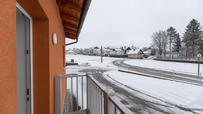Blick vom Balkon auf eine verschneite Landschaft mit Häusern und Bäumen im Hintergrund.