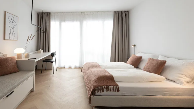 Helles Schlafzimmer mit modernem Design, Parkettboden und Zugang zu großen Fenstern.