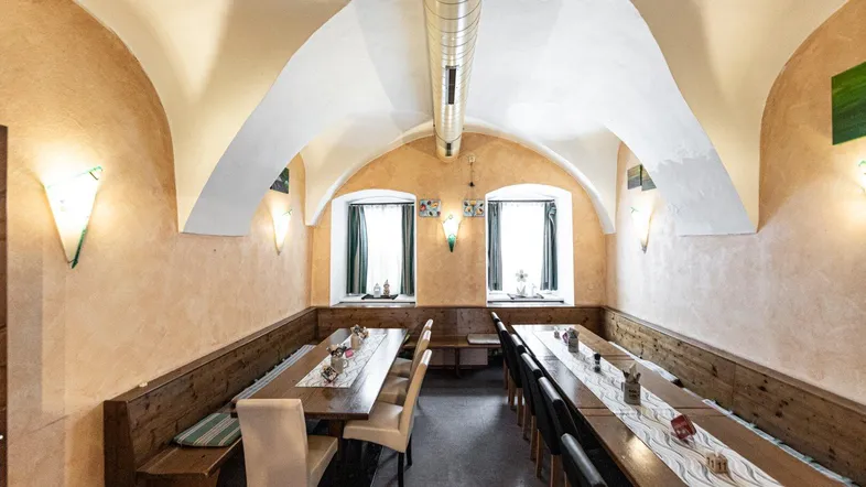 Langer Speisesaal mit Gewölbedecke, Holzbänken und zwei Fenstern, die natürliches Licht hereinlassen.