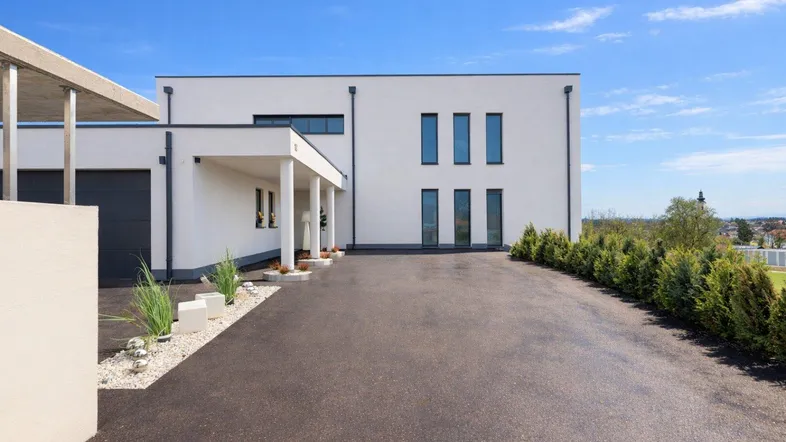 Moderne Hausfassade mit Einfahrt und Garage, umgeben von gepflegten Hecken und Kiesbeeten.