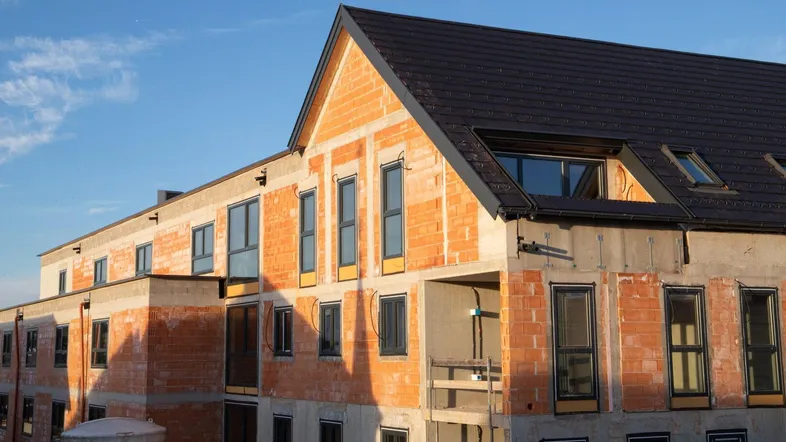 Neubau im Rohbauzustand mit Ziegelwänden und Dachkonstruktion unter blauem Himmel.