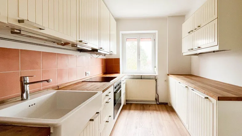 Helle Küche mit cremefarbenen Einbauschränken, Holzarbeitsplatten, integrierten Geräten und Fenster mit Blick nach draußen.