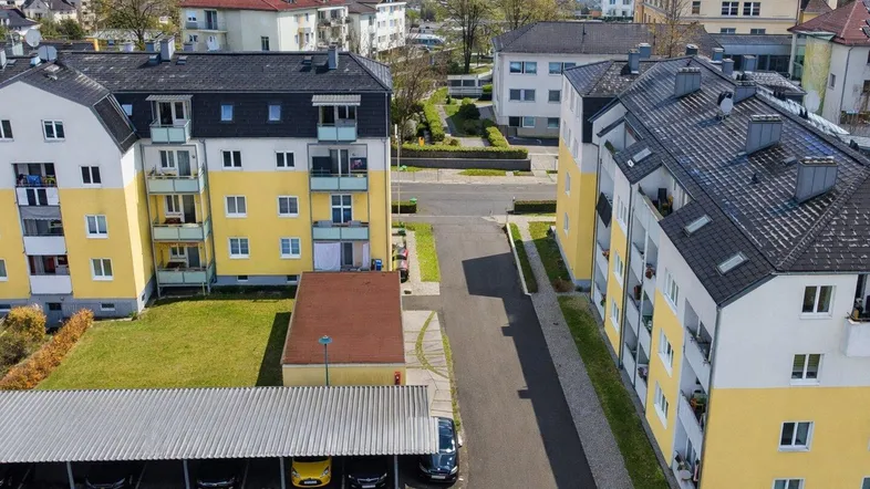 Luftaufnahme von Mehrfamilienhäusern mit Balkonen, Grünflächen und überdachten Parkplätzen.