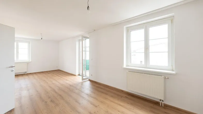 Helles, unmöbliertes Wohnzimmer mit Laminatboden und Zugang zu einem Balkon.