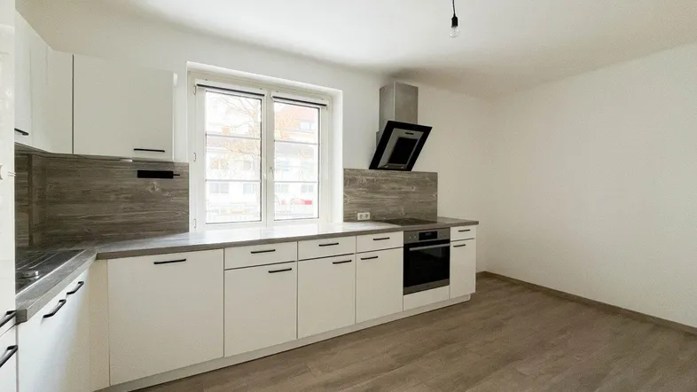 Moderne Küche mit weißen Schränken, integriertem Backofen und Dunstabzugshaube, bereit zur Einrichtung.