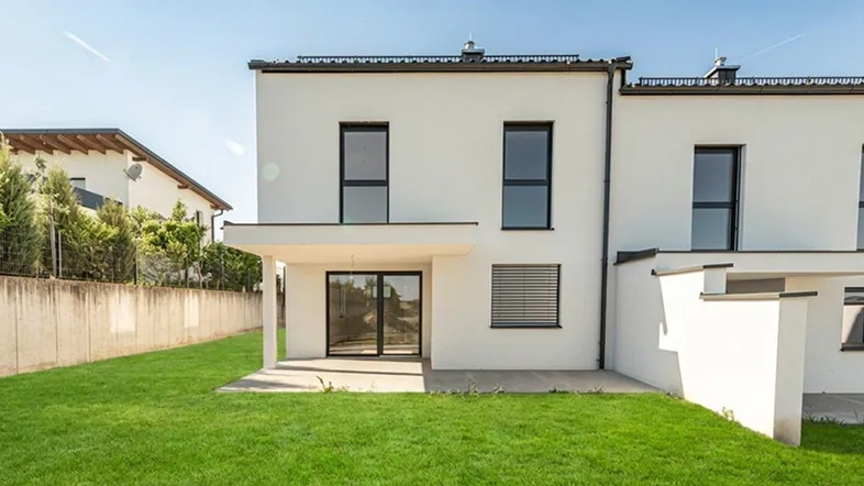 Moderne Reihenhausfassade mit weißem Putz, großen Fenstern und einer grünen Rasenfläche.