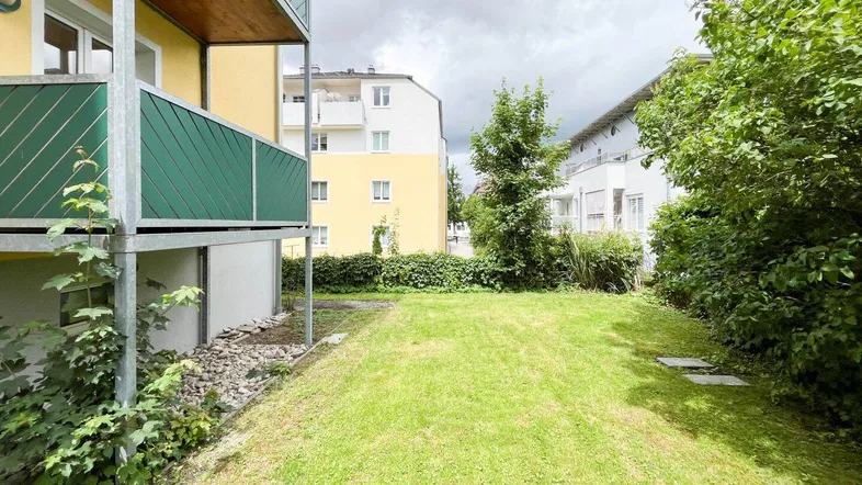 Gebäudeansicht mit Rasenfläche und Balkonen, umgeben von Bäumen und Sträuchern.