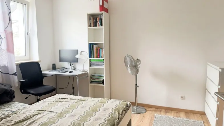 Helles Schlafzimmer mit Holzboden, Schreibtisch und einem Bücherregal, ideal für Studenten oder Singles.