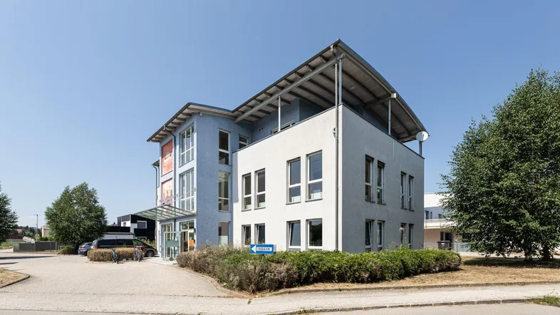 Modernes Geschäftsgebäude mit geschwungenem Dachüberstand und Parkplätzen unter blauem Himmel.