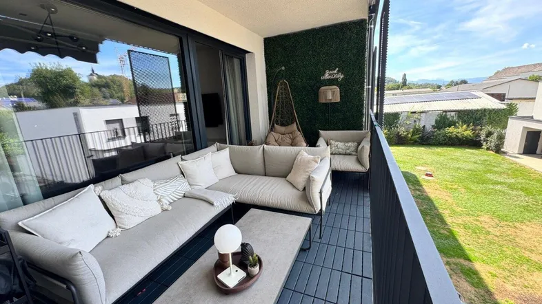 Geräumiger Balkon mit bequemen Outdoor-Möbeln, Kunstrasenwand und Blick ins Grüne.