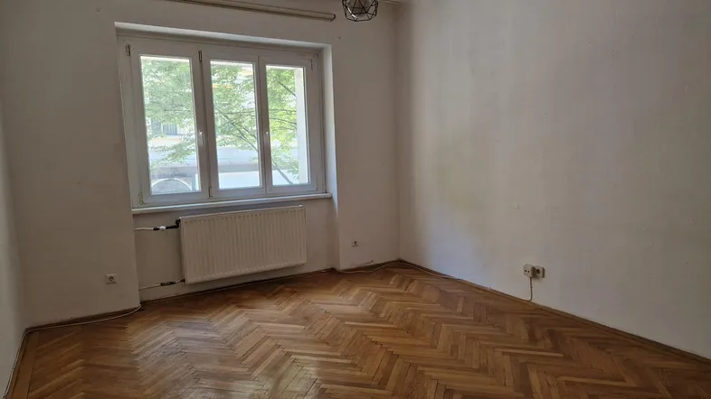 Helles Zimmer mit Fischgrätparkettboden und großem Fenster, das viel Tageslicht hereinlässt.