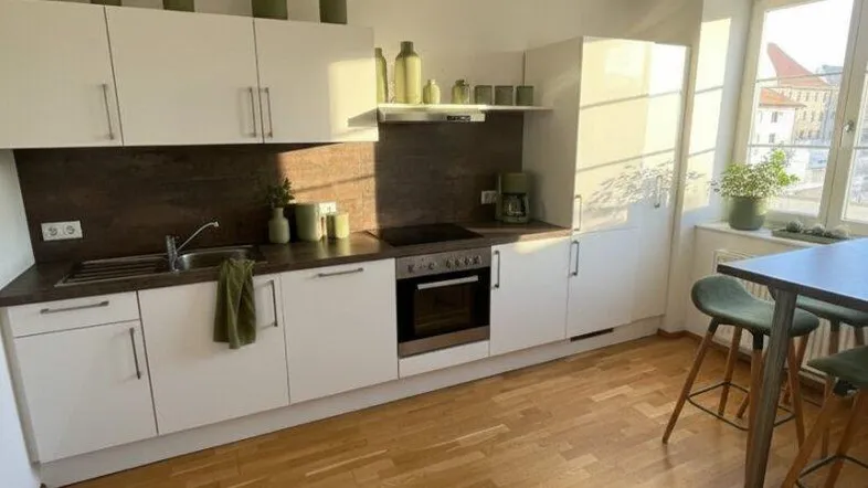 Moderne Küche mit weißen Schränken, Holzboden und viel Tageslicht durch das Fenster.