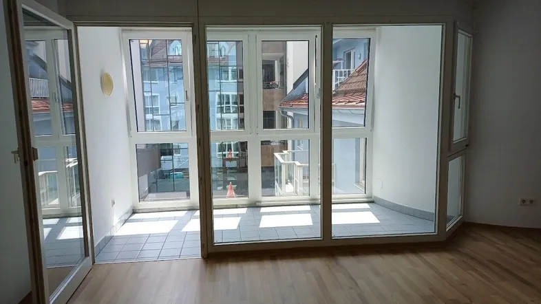 Helles Zimmer mit Parkettboden und Zugang zu einem kleinen Balkon mit Stadtblick.