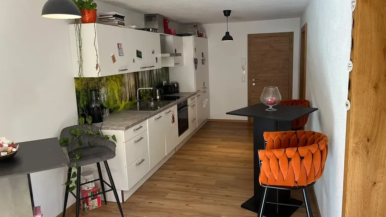 Moderne Küche mit weißen Schränken, Waldmotiv-Rückwand und Bartisch mit Hockern.