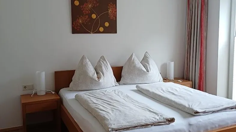 Helles Schlafzimmer mit Doppelbett, Holzboden und einfacher Dekoration, ideal für erholsame Nächte.