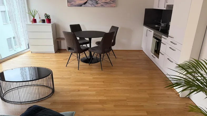 Heller offener Wohn-Essbereich mit integrierter Küche, Holzboden und Zugang zum Balkon.