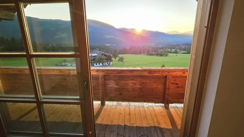 Sonnenuntergang über einem grünen Tal mit Bergblick, gesehen von einem Holzbalkon.