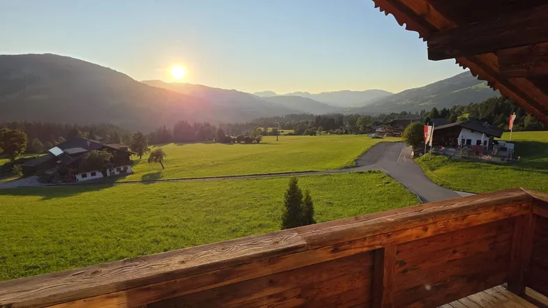 Sonnenuntergang über einer malerischen Berglandschaft, gesehen von einem rustikalen Holzbalkon mit weitem Blick.