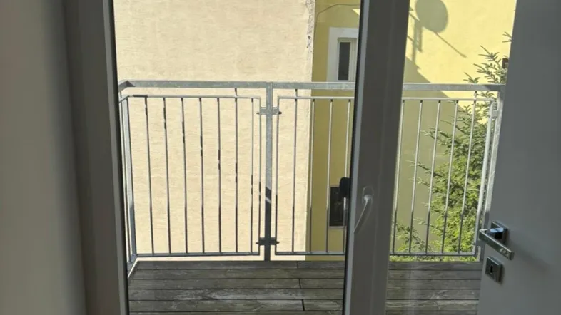 Heller Zugang zu einem Holzbalkon mit Metallgeländer und Blick auf umliegende Gebäude.