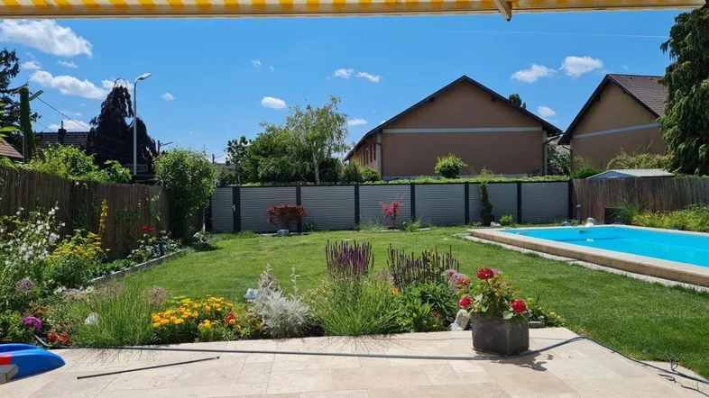 Sonniger Gartenbereich mit Pool, gepflegtem Rasen und einer gefliesten Terrasse unter einer Markise.