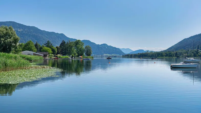 Seeufer mit ruhigem Wasser, umgeben von grünen Bergen unter klarem Himmel.