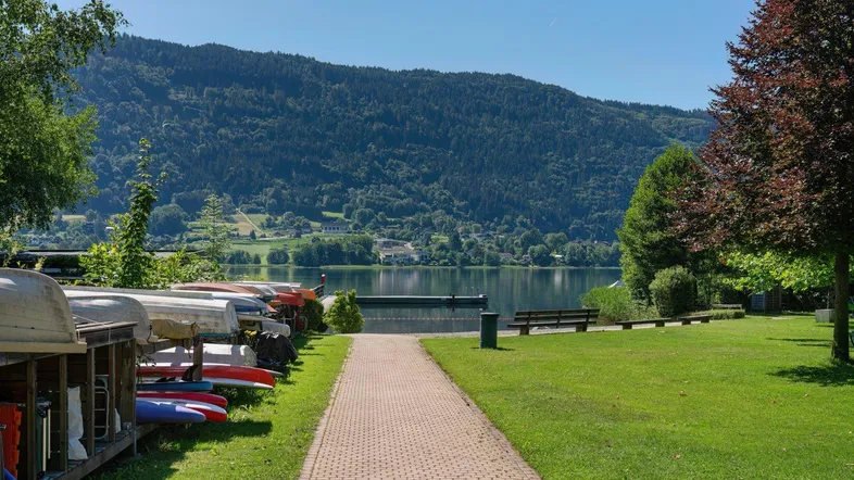 Idyllischer Seeblick mit Bootsanlegestelle, umgeben von grünen Wiesen und bewaldeten Bergen.