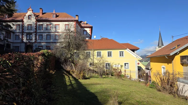 Traditionelle Gebäude mit Ziegeldächern und einem grünen Hang unter blauem Himmel.