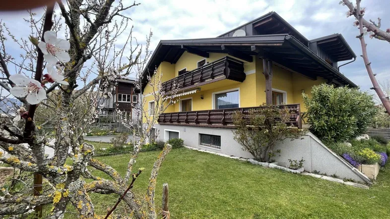 Gelbes Haus mit traditionellen Holzbalkonen und gepflegtem Gartenbereich im Frühling.