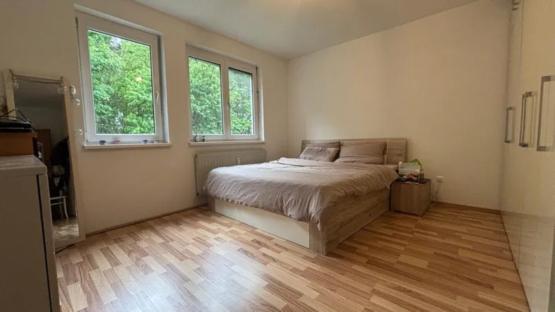 Helles Schlafzimmer mit Laminatboden, großem Fenster und Blick ins Grüne.