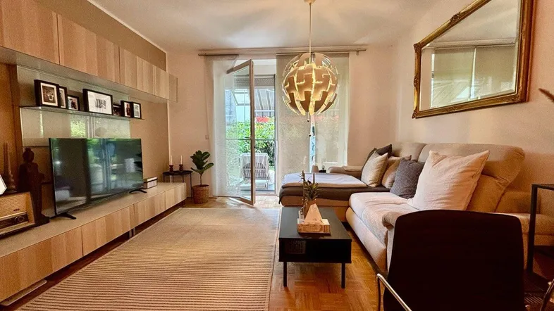 Gemütliches Wohnzimmer mit Parkettboden, Sofa und Zugang zu einer Terrasse oder Garten.