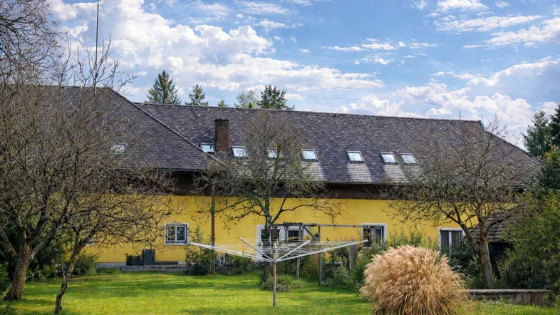 Großer grüner Garten mit Wäschespinne und Blick auf das gelbe Gebäude mit Dachfenstern.