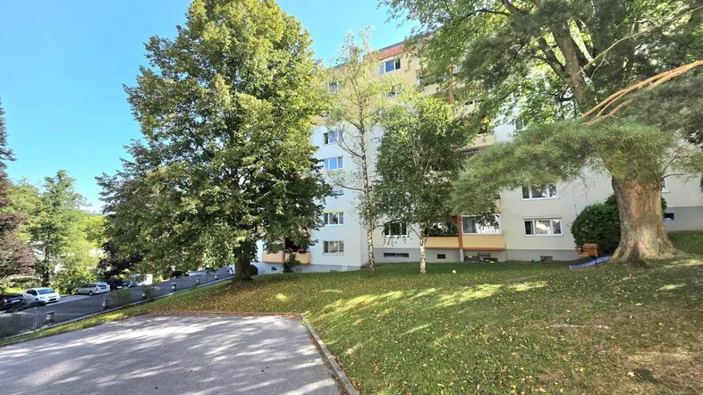 Mehrfamilienhaus mit Grünfläche und Bäumen in einer ruhigen Wohngegend.