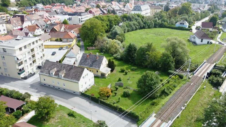 Luftaufnahme einer ländlichen Stadtansicht mit Wohngebäuden, Grünflächen und Bahngleisen.