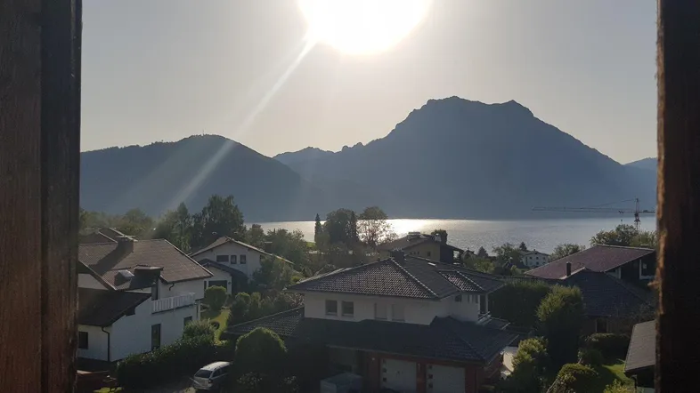 Sonnenaufgang über dem See mit Bergen im Hintergrund, gesehen durch ein Fenster.