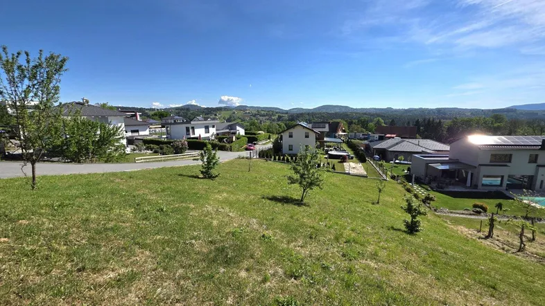Weitläufige Grünfläche mit Blick auf moderne Häuser und die umliegende Landschaft unter blauem Himmel.