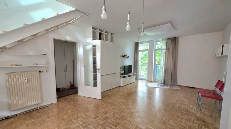 Helles Wohnzimmer mit Parkettboden, offener Treppe und Zugang zu einem Balkon.