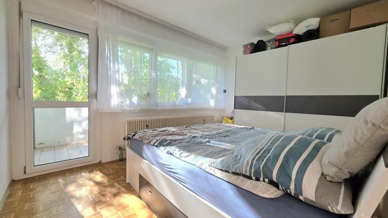 Helles Schlafzimmer mit Parkettboden, großem Kleiderschrank und Zugang zum Balkon.