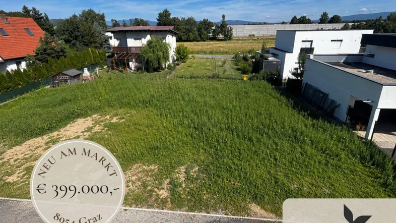 Ungenutztes Grundstück mit weitem Blick und umliegenden Häusern unter blauem Himmel.