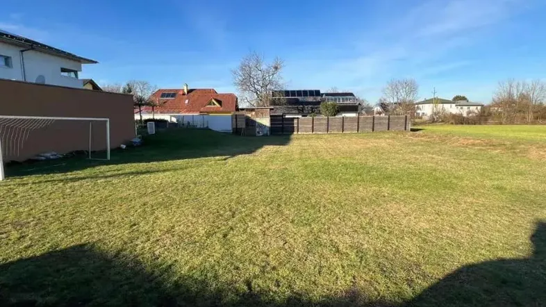 Große Rasenfläche mit Fußballtor und angrenzenden Wohnhäusern unter blauem Himmel.