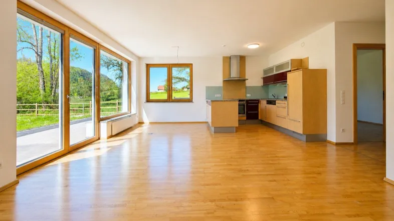 Helles, offenes Wohn-Esszimmer mit Holzboden, großen Fenstern und integrierter Küche.