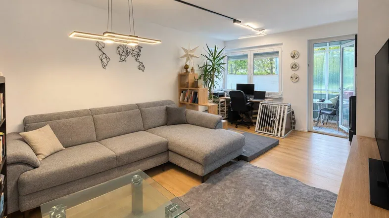 Helles Wohnzimmer mit gemütlichem Ecksofa, Holzboden und Zugang zu einem Balkon.