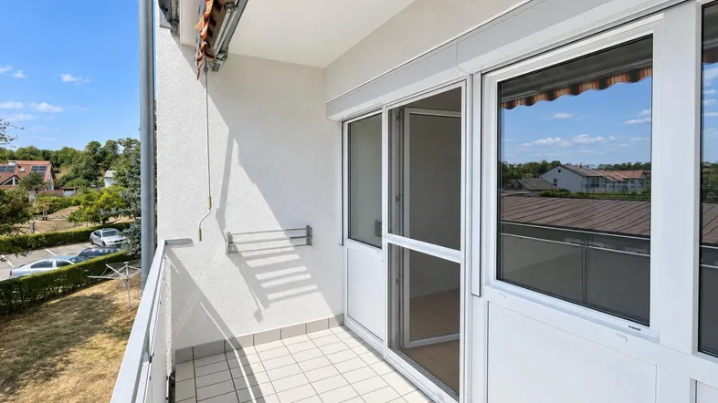 Heller Balkon mit Fliesenboden, Wäscheständer und Blick auf die Umgebung.