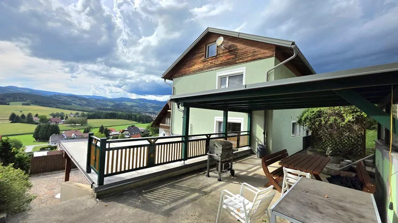 Große überdachte Terrasse mit Grillplatz und weitem Blick über die grüne Landschaft.