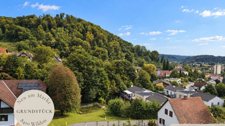 Landschaftliche Ansicht mit Häusern, grünen Hügeln und einem Grundstück in ländlicher Umgebung.