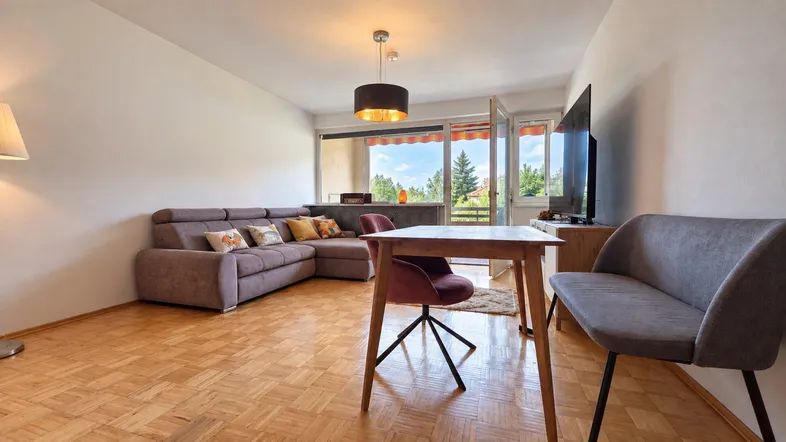 Helles Wohn- und Esszimmer mit Parkettboden, gemütlichem Sofa und Zugang zum Balkon.