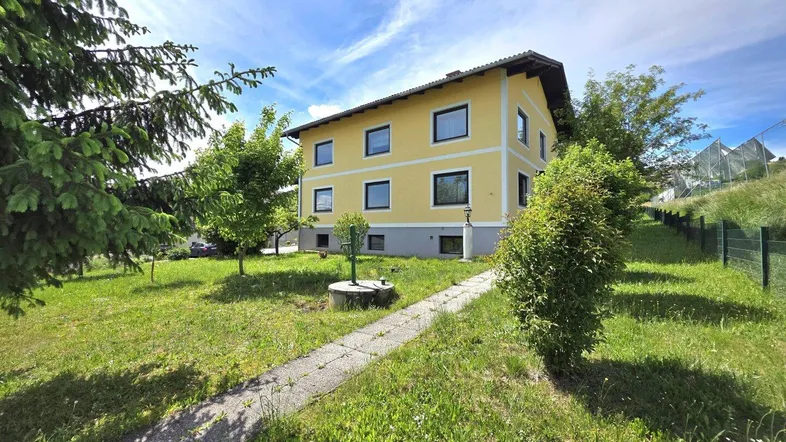 Gelbes Einfamilienhaus mit grünem Garten und gepflegtem Rasen unter blauem Himmel.