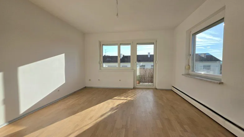 Helles Wohnzimmer mit Parkettboden, weißen Wänden und Zugang zu einem kleinen Balkon.
