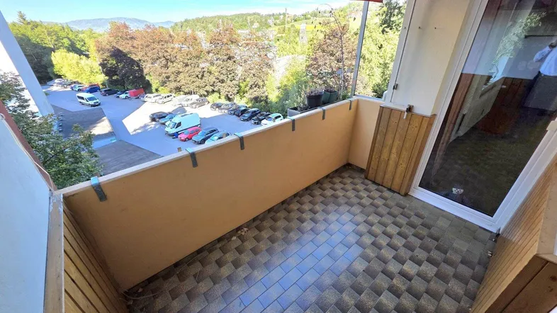 Geräumiger Balkon mit Blick auf die Umgebung und Parkplätze, ausgestattet mit einem roten Sonnenschutz.