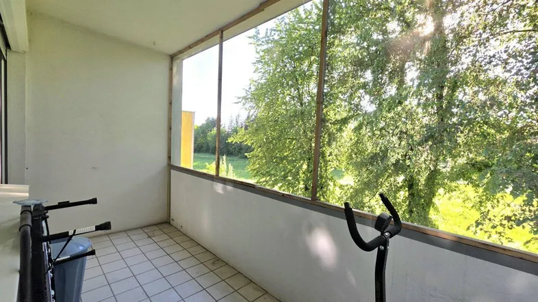 Heller, verglaster Balkon mit Fliesenboden und Blick ins Grüne, ideal für Sportgeräte.